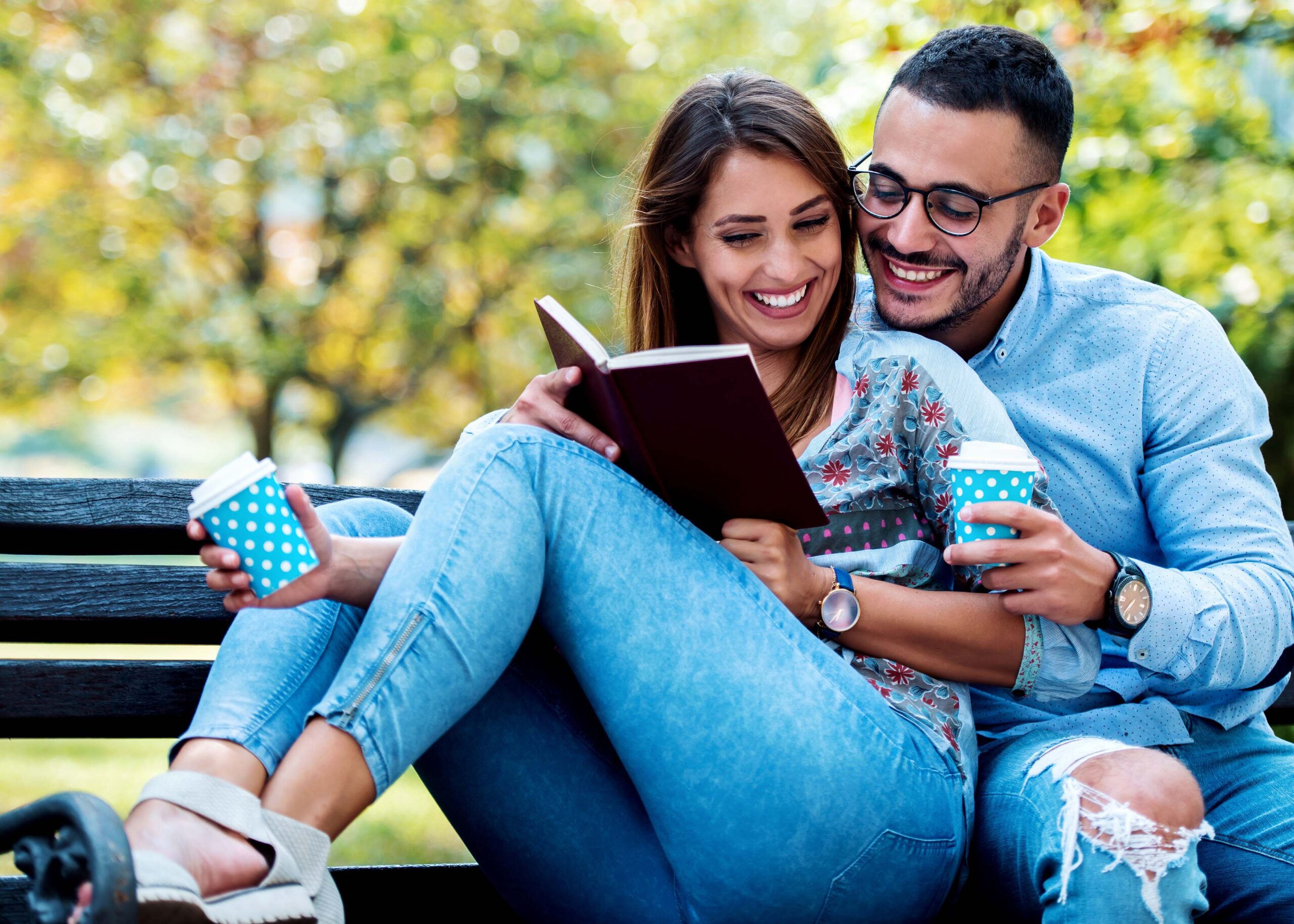 couple sitting on a bench smiling and reading a book
