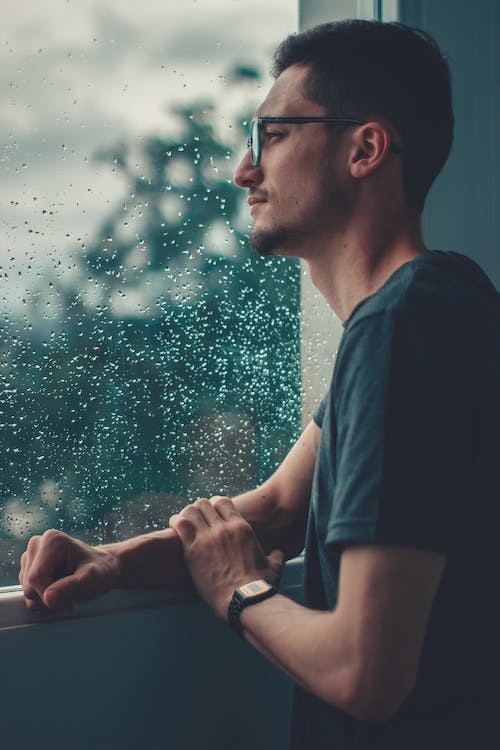 Man looking out rainy window looking sad