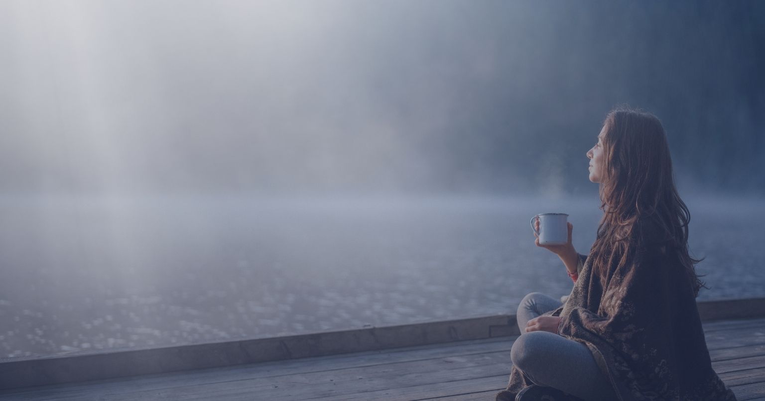 Person sitting by a lake holding a cup, representing mindfulness after therapy