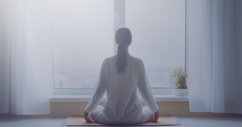 A person practicing meditation near a window, symbolizing inner peace and anxiety relief.